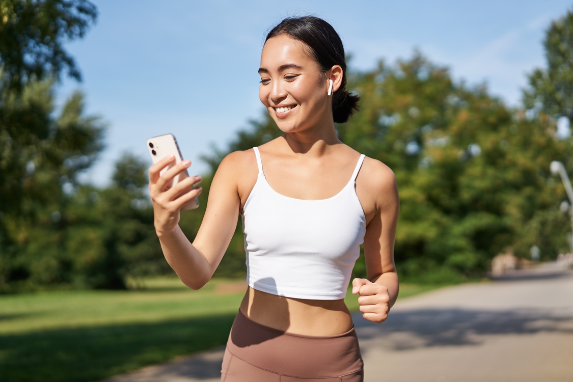 Uma mulher correndo em um parque, olhando para o celular enquanto usa um aplicativo de assessoria de corrida. Uma mulher correndo em um parque, olhando para o celular enquanto usa um aplicativo de assessoria de corrida.