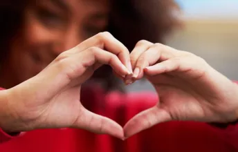 Pessoa faz gesto de coração com as mãos, simbolizando os cuidados com a saúde do coração por meio da avaliação de um(a) cardiologista e de exames cardíacos.